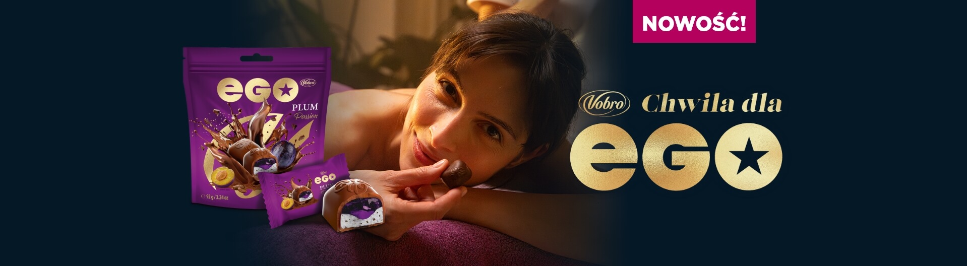 Kobieta leży na brzuchu podczas masażu i z delikatnym uśmiechem trzyma przy ustach czekoladową pralinkę. Obok widoczne jest fioletowe opakowanie EGO Plum Passion, przekrojona pralina z nadzieniem śliwkowym oraz hasło „NEW! Vobro. A moment for EGO” na ciemnym tle.